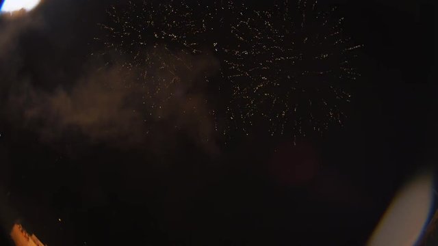Fireworks display with closer explosions at upper and lower left of frame raining debris