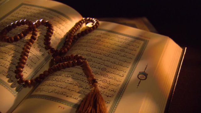 Wooden prayer beads lying across close-up pages of an open Quran