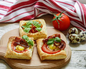 Open pies of puff pastry with quail egg, tomatoes, bacon and Basil. Breakfast. Selective focus

