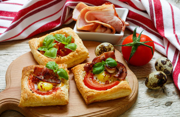 Open pies of puff pastry with quail egg, tomatoes, bacon and Basil. Breakfast. Selective focus

