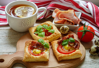 Open pies of puff pastry with quail egg, tomatoes, bacon and Basil. Breakfast. Selective focus
