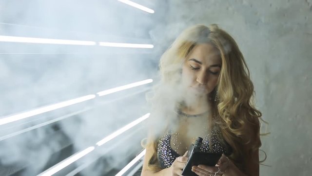 Sexy blonde woman dressed in black transparent dress smokes and reads tablet