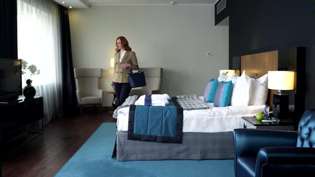 Hotel Room for Businesswomen/Business woman with a Red hair  enters a room. The suitcase and handbag in her hand. She sits down on the bed in anticipation of a comfortable stay at the hotel