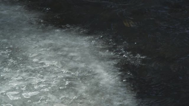 Close-up of a stream flowing under and over a thin crust of ice