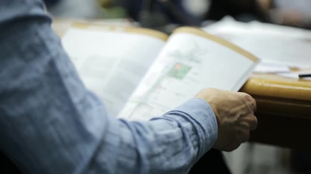 Man sitting at conference leafing through a magazine with charts and drawings.