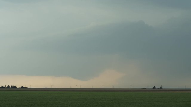 Small funnel cloud descending below cloud mass hanging over prairie farmland