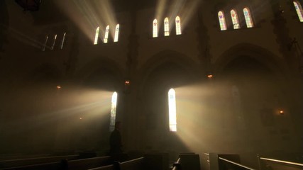 Priest walking down the aisle in darkened nave of Catholic church