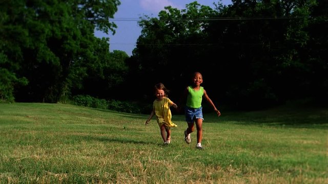 Two little girls running hand in hand across grass toward camera