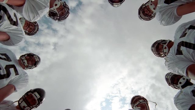 Football players in a huddle, camera looking up from center