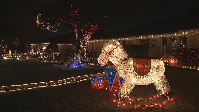 An illuminated rocking horse and other Christmas lights decorating neighboring houses