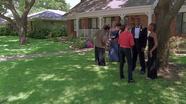 Parents admiring two teenage couples in prom clothes on lawn of suburban house