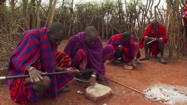 Four young Masai men sharpening knives and smoothing spear shafts