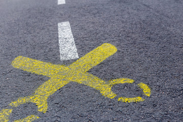 Yellow scissors painted at asphalt road with white line