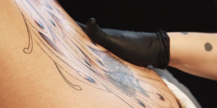 Gloved hand wipes oil onto a tattoo on a woman's back