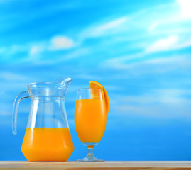 Orange juice in jug and glass on sky background