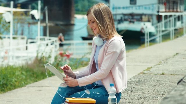 Young adult woman with headphones using tablet pc outdoors near river