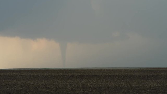 Slender tornado from wall cloud advancing over plowed fields, time lapse