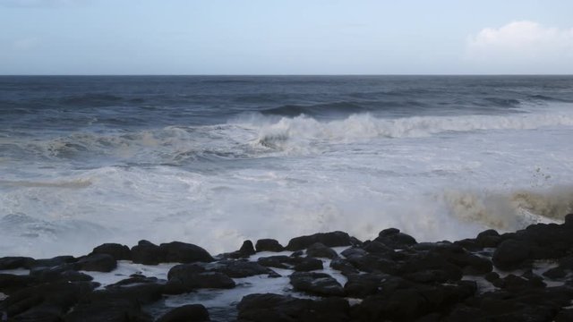 Foaming waves crashing over dark rocks close to the camera