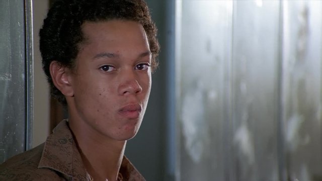 Portrait of an unsmiling curly-haired teenage boy standing near school lockers