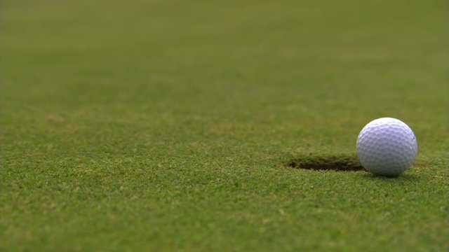 Golf ball rolling from left toward and just past close-up hole at right of frame