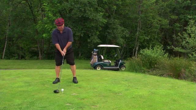 Golfer in plaid cap approaching ball on tee and driving it out of frame to right