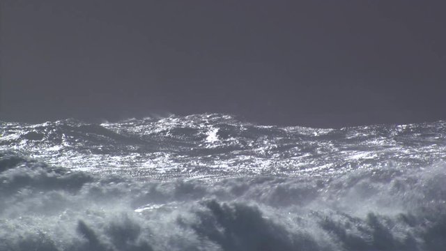Silver-capped waves cresting and breaking into spray under gray sky
