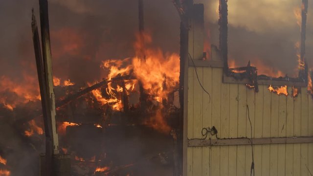 Flames consume charred rubble inside a house destroyed by fire