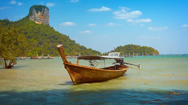 3840x2160 video - Beautifully handcrafted, wooden longtail boat, riding at anchor in the silty, tropical water, beneath a towering limestone outcrop.
