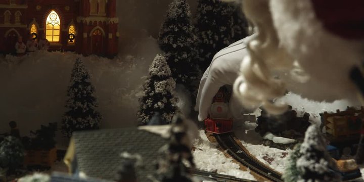 A tabletop Christmas village; Santa's hand setting toy train in motion