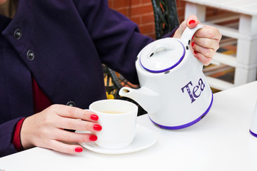 Woman with red nail polish pouring a tee in a cup in a cafee outdoors