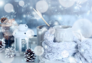 Cup of hot drink in on the windowsill in living room. Comfortable winter weekend or holidays at home. Snow effect