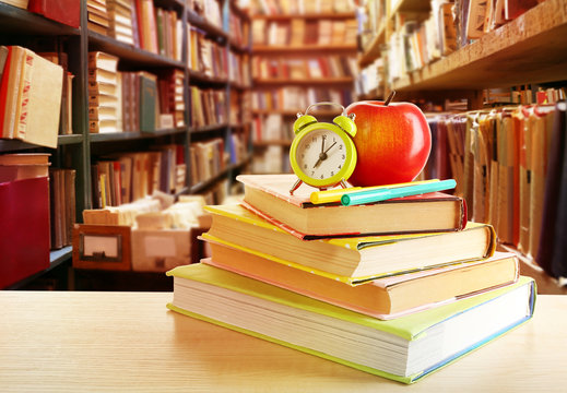 Books, alarm clock and apple on blurred library background