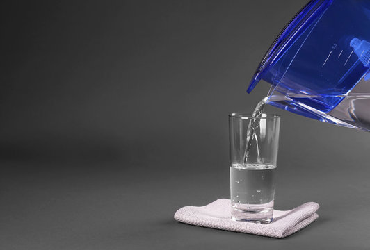 Purified water pouring into glass on grey background