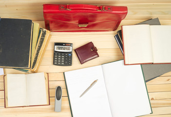 On a wooden table books, documents, calculator, red briefcase.