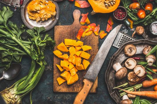 Chopped Pumpkin on rustic cutting board with kitchen knife and mushrooms and vegetables ingredients  for tasty vegetarian cooking, dark styled,  top view