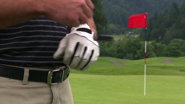 Golfer adjusting glove, taking putter, and walking out of frame at left