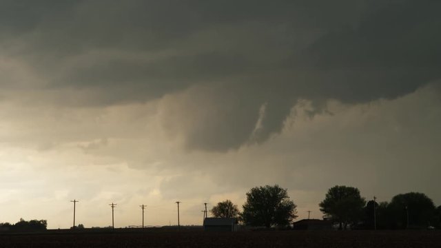 Time-lapse gray clouds hint at funnel shapes above a prairie farm at twilight