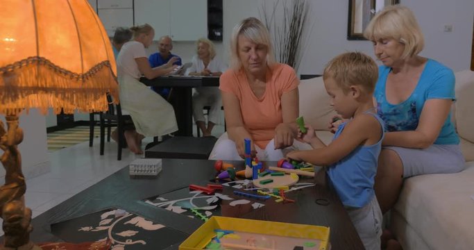 Little boy and two grandmothers playing with construction kits and toy vegetables at home