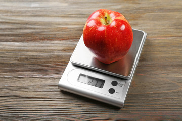 Apple with digital kitchen scales on wooden background