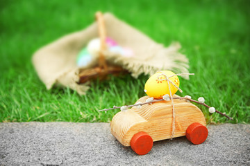 Decorative toy car with pussy willow and Easter egg on green grass background