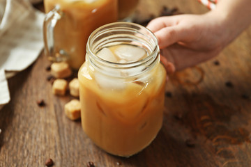 Woman holding iced coffee drink on wooden table background