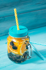 Detox water cocktail with orange and blueberries on blue wooden background