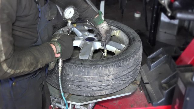 dirty worker hands inflate tire air wit compressor on mounting machine.