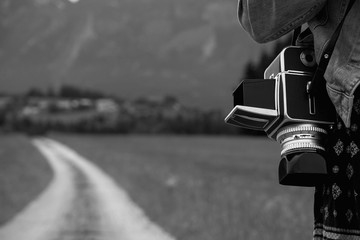 Frau mit einer alten, analogen 6x6cm Mittelformatkamera geht auf einem Feldweg