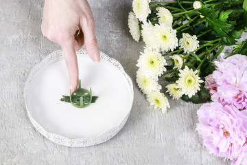 Woman applying modelling clay and pinholder on flower stand.