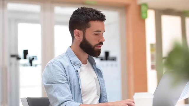 Trendy bearded guy in office working on laptop