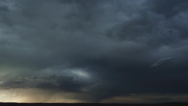 Heavy gray clouds flow across prairie as rain falls along dark horizon, time lapse