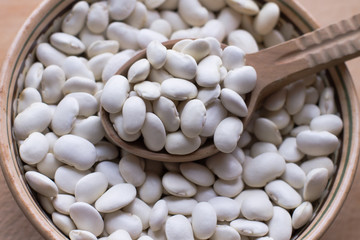 White uncooked beans in a pot with a wooden spoon