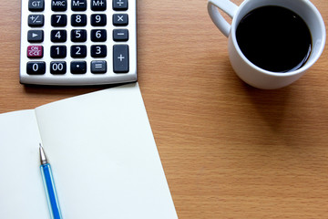 Notebook with pen, calculator and white cup of coffee