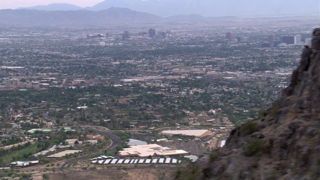 Wide view of distant downtown Phoenix and outlying areas, rocky peak through frame. Shot in 2007.
